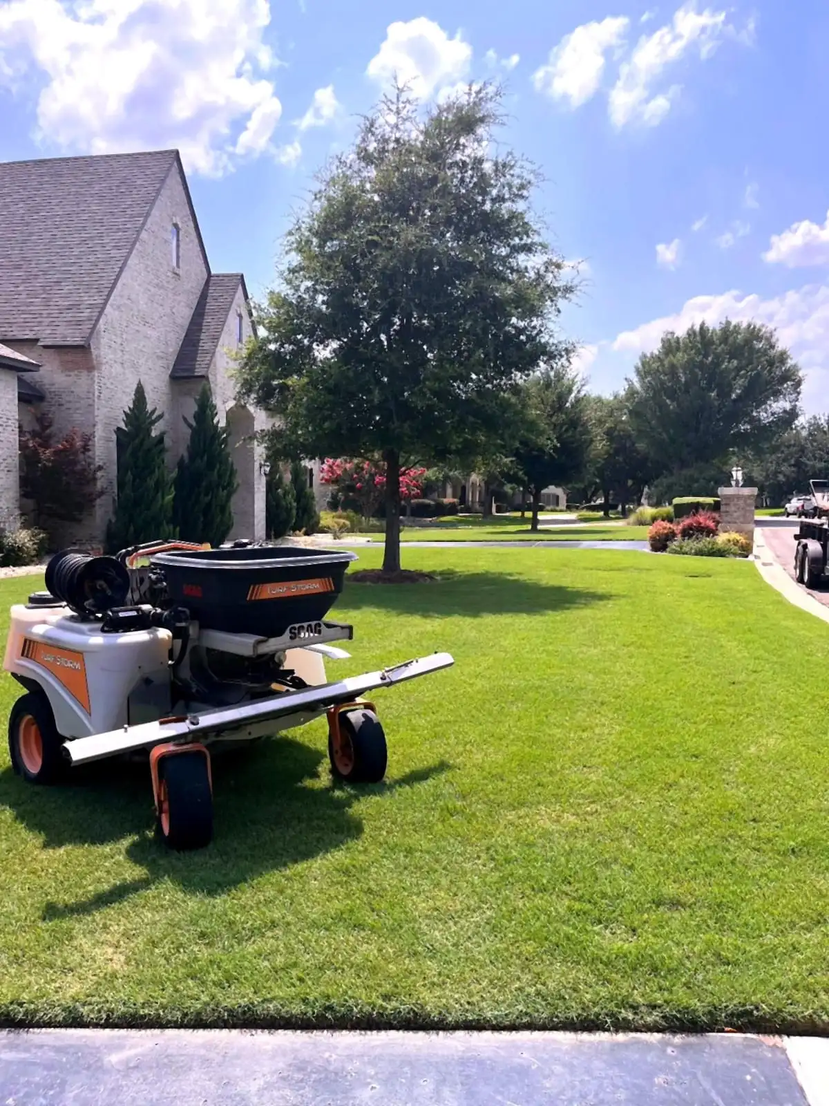 A zero-turn mower on a striped, freshly cut residential lawn maintained by H&M.