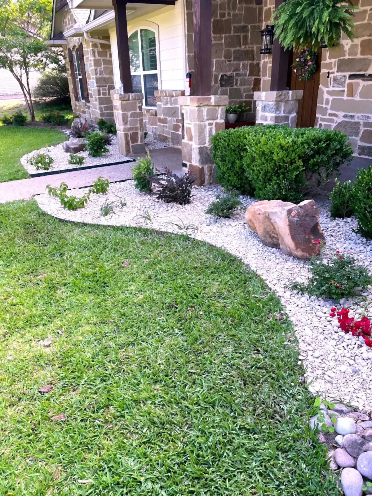Stone home with white rock beds, shaped shrubs, boulder accent, and flowering color.