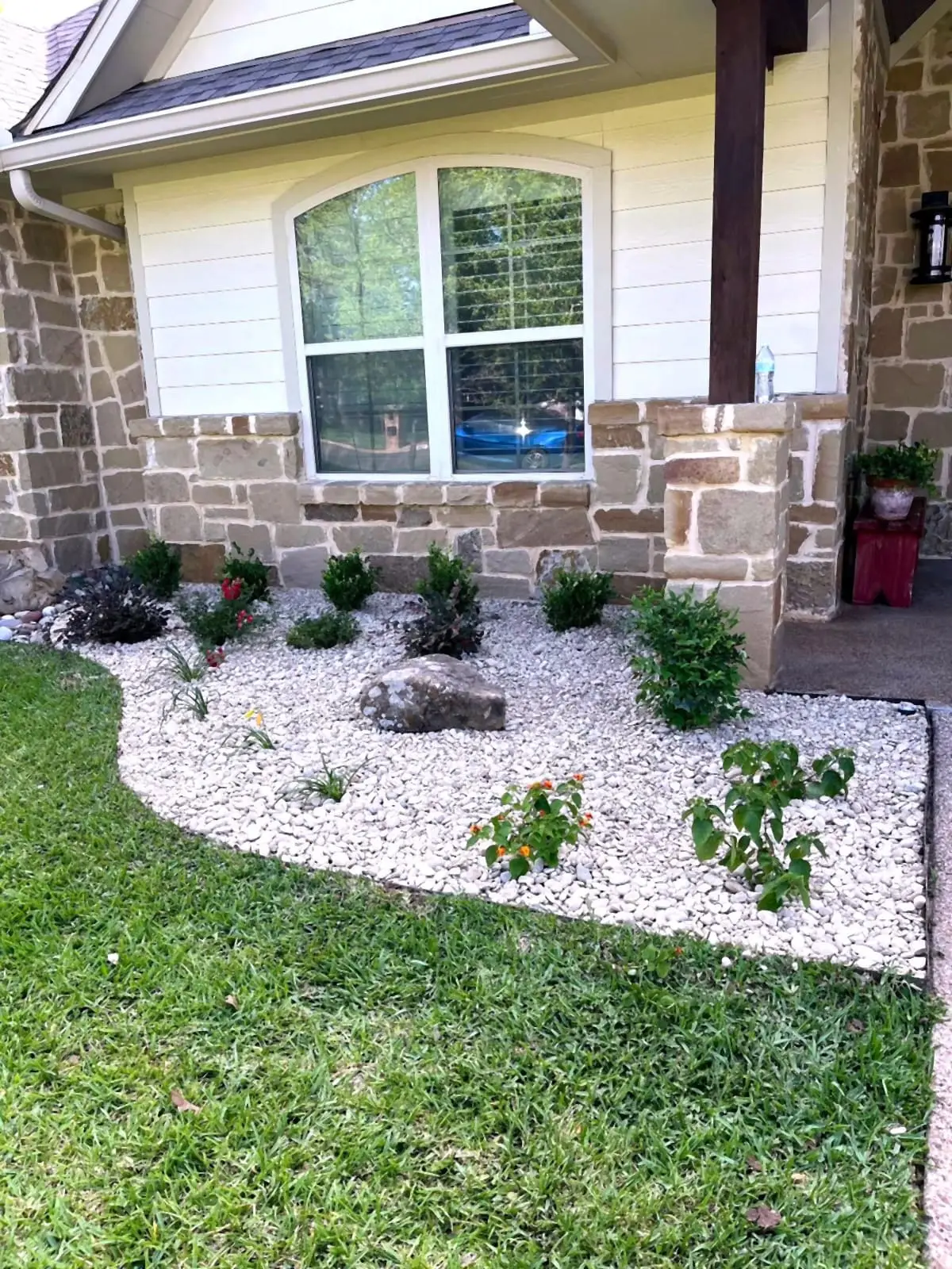 Foundation bed under an arched window with white rock, boulders, and flowering plants.
