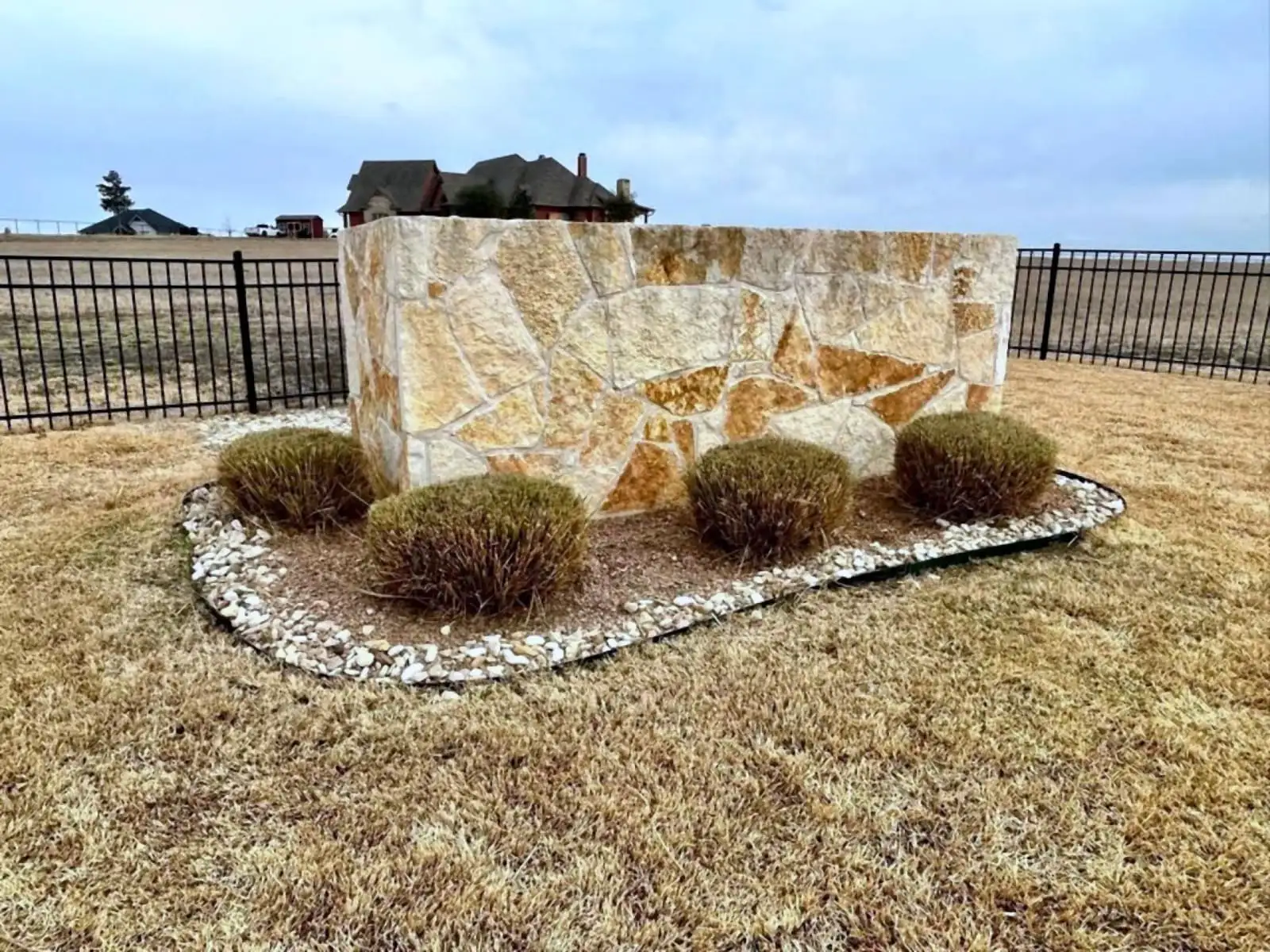 A stone entry monument with a river rock border and ornamental grasses installed by H&M.